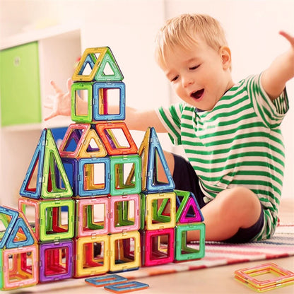  Enfant assis sur un tapis devant une construction multicolore en pièces magnétiques carrées et triangulaires .